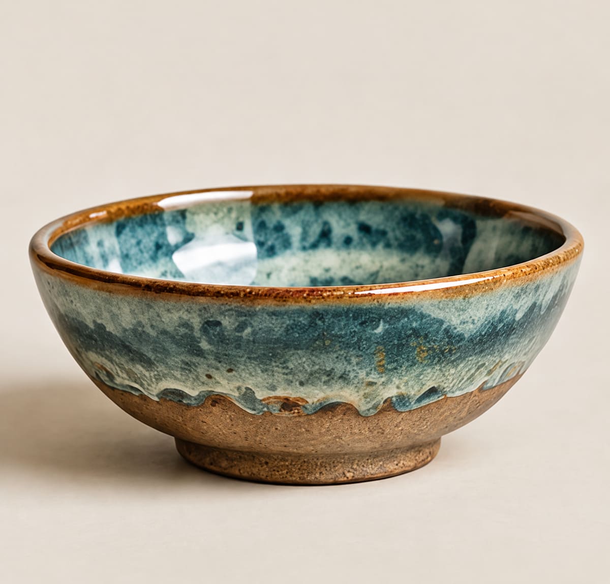 Shallow handmade bowl glazed in teal and blue with a brown rim